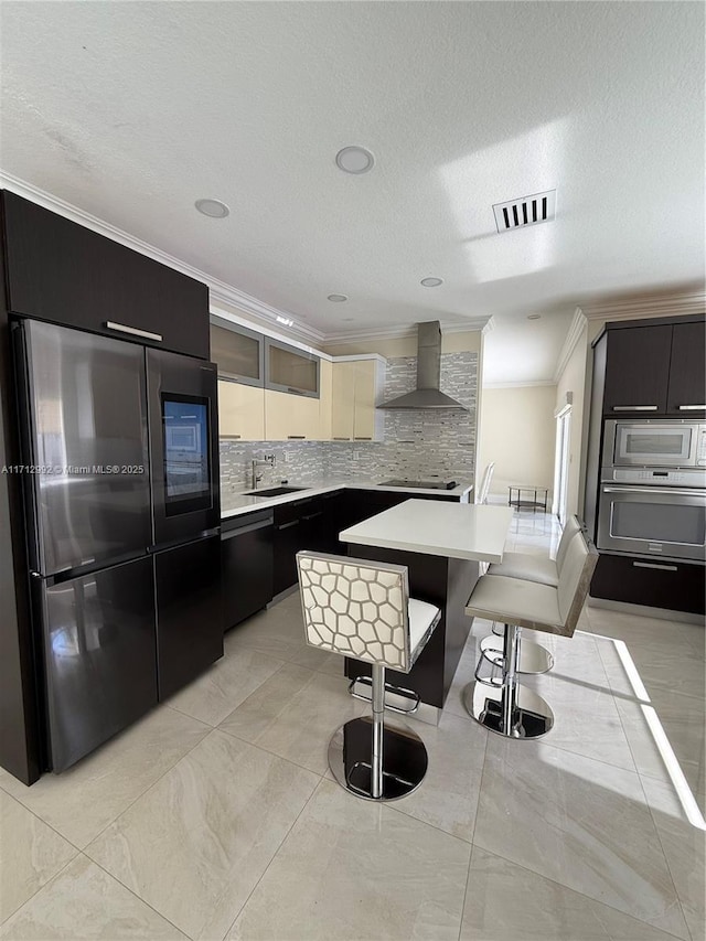 kitchen featuring a kitchen bar, wall chimney exhaust hood, stainless steel appliances, crown molding, and a kitchen island