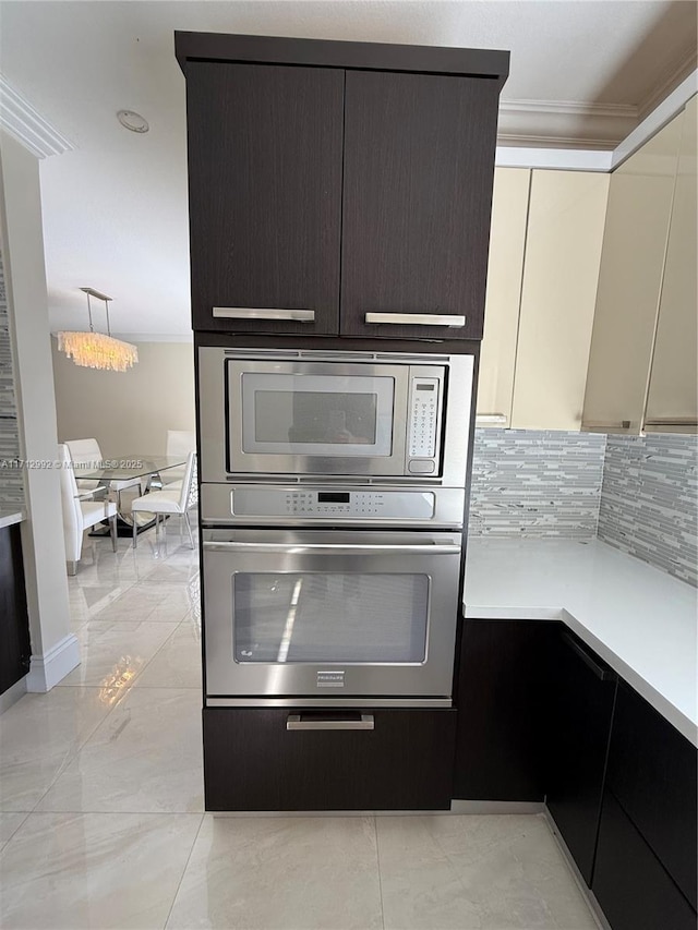 kitchen with hanging light fixtures, decorative backsplash, ornamental molding, appliances with stainless steel finishes, and cream cabinetry