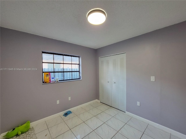 unfurnished bedroom with light tile patterned flooring, a textured ceiling, and a closet