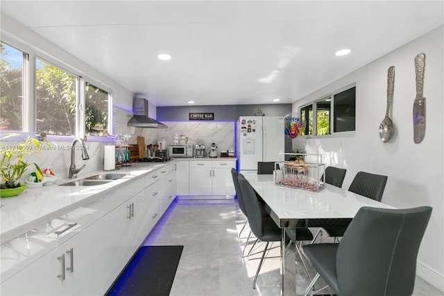 kitchen featuring white cabinetry, sink, wall chimney exhaust hood, backsplash, and white appliances