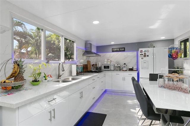 kitchen with sink, wall chimney range hood, white appliances, decorative backsplash, and white cabinets