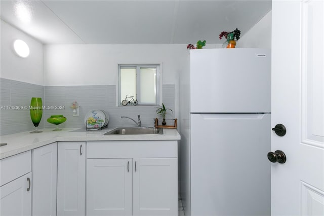 kitchen featuring white refrigerator, backsplash, white cabinetry, and sink