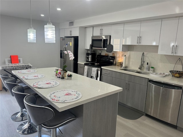 kitchen featuring a breakfast bar, sink, hanging light fixtures, light hardwood / wood-style flooring, and stainless steel appliances