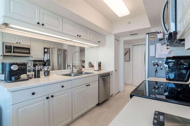 kitchen with appliances with stainless steel finishes, a raised ceiling, sink, light tile patterned floors, and white cabinetry