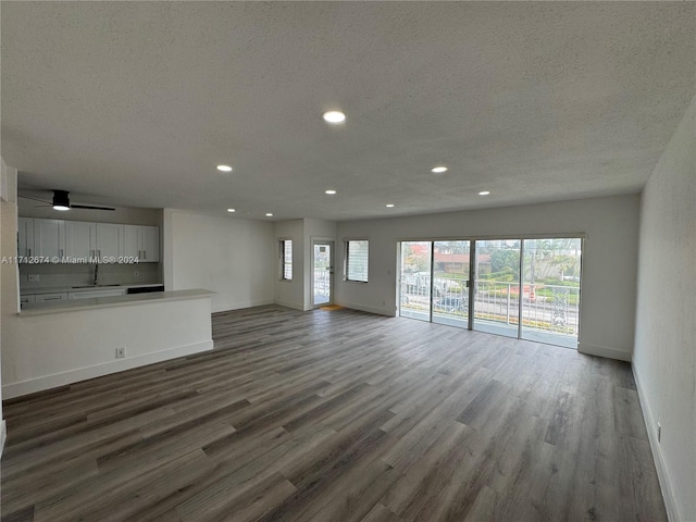 unfurnished living room with plenty of natural light, ceiling fan, wood-type flooring, and a textured ceiling