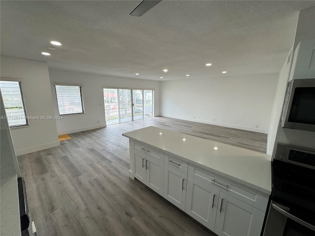 kitchen with white cabinets, light stone countertops, a textured ceiling, wall oven, and light hardwood / wood-style floors