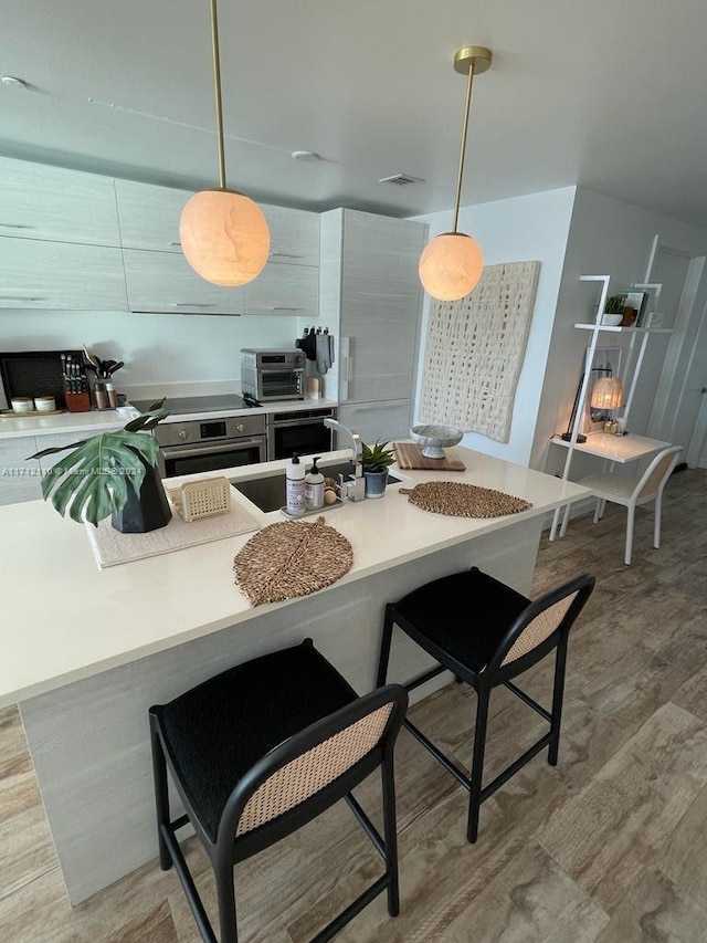 kitchen with a kitchen breakfast bar, oven, pendant lighting, and light wood-type flooring