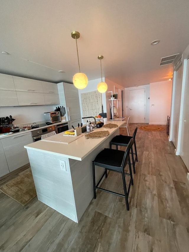 kitchen with a spacious island, light hardwood / wood-style flooring, decorative light fixtures, a kitchen bar, and white cabinetry