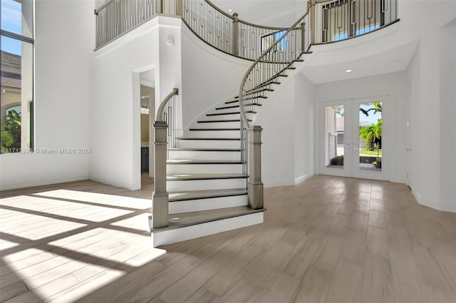 entrance foyer with french doors, a towering ceiling, and light hardwood / wood-style flooring