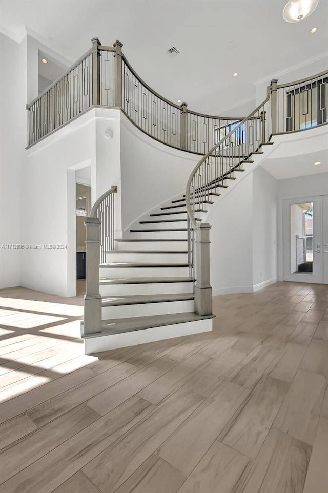 stairway featuring french doors, wood-type flooring, a high ceiling, and ornamental molding