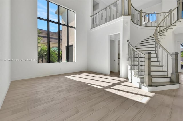 unfurnished living room featuring a wealth of natural light, light wood-type flooring, and a high ceiling