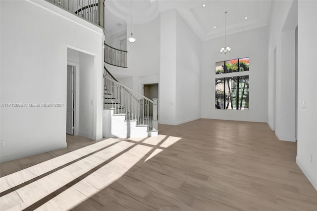 unfurnished living room featuring a towering ceiling, light hardwood / wood-style flooring, and a notable chandelier