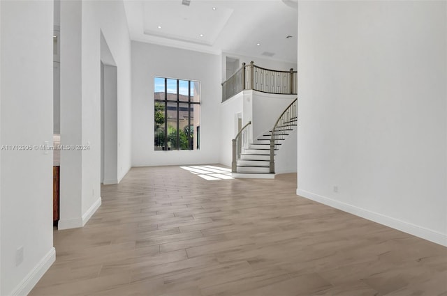 interior space with a tray ceiling, light hardwood / wood-style flooring, and a towering ceiling