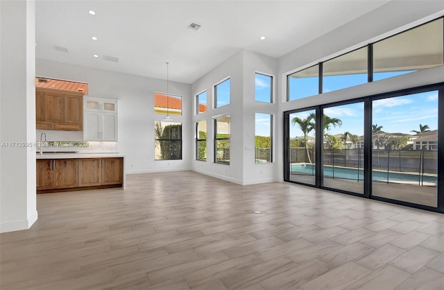 unfurnished living room with a healthy amount of sunlight, a high ceiling, and light hardwood / wood-style flooring