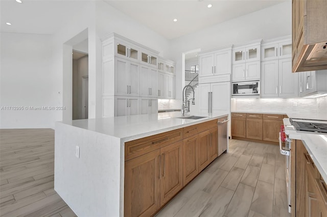 kitchen featuring white cabinetry, sink, stainless steel appliances, a large island with sink, and light wood-type flooring