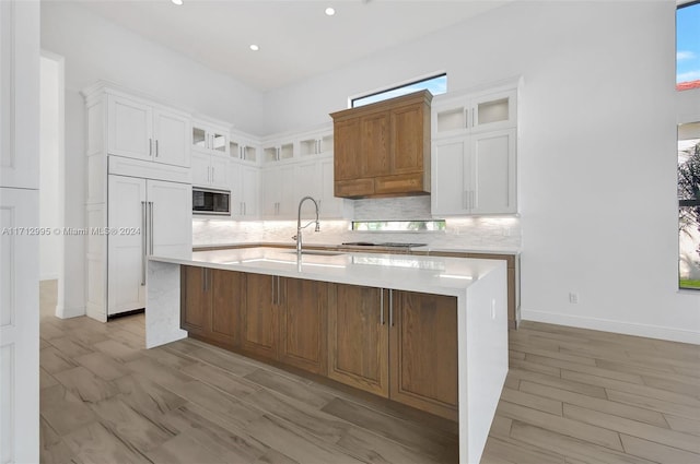 kitchen featuring a large island with sink, decorative backsplash, built in appliances, and white cabinets