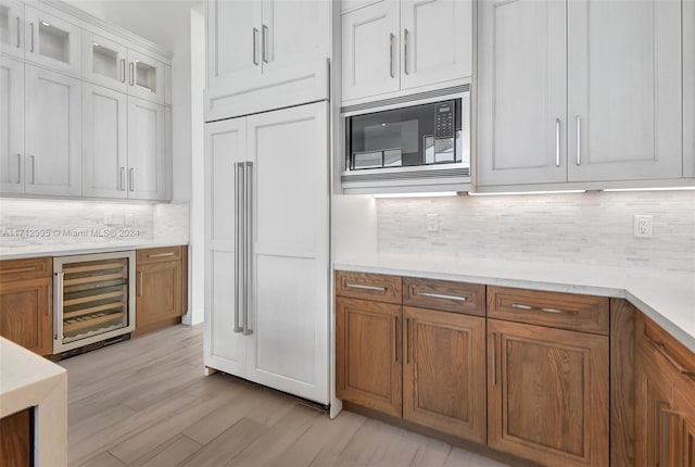 kitchen featuring beverage cooler, light hardwood / wood-style flooring, backsplash, built in appliances, and white cabinets