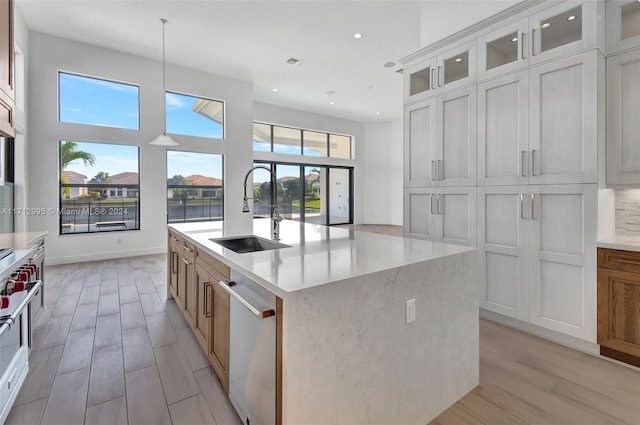 kitchen featuring sink, pendant lighting, a center island with sink, dishwasher, and white cabinets