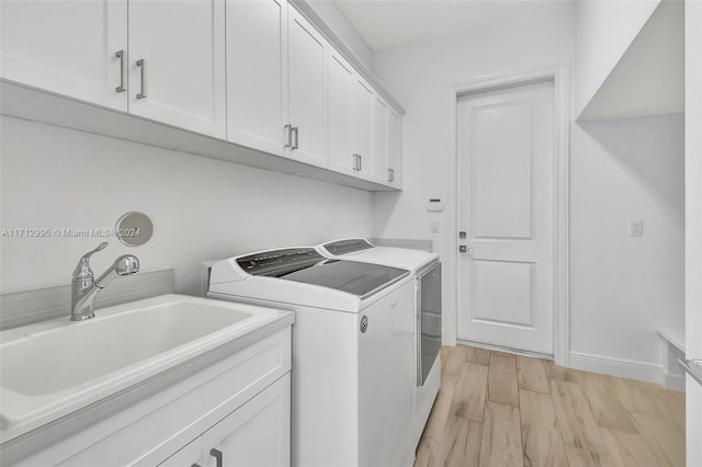 clothes washing area featuring washing machine and dryer, cabinets, sink, and light hardwood / wood-style floors