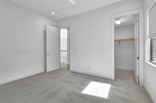 unfurnished bedroom with a walk in closet, light colored carpet, and a closet