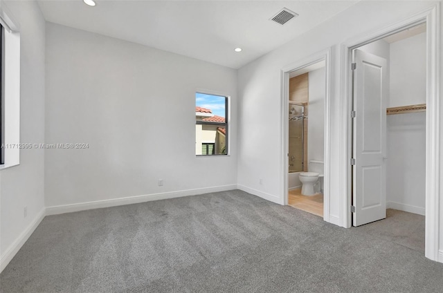 unfurnished bedroom with a walk in closet, light colored carpet, a closet, and ensuite bathroom