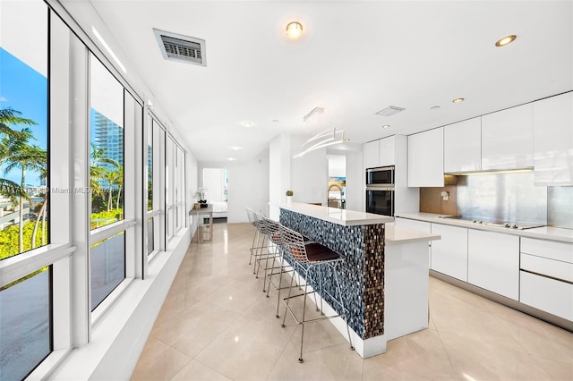 kitchen featuring a breakfast bar, stainless steel microwave, white cabinets, oven, and a kitchen island