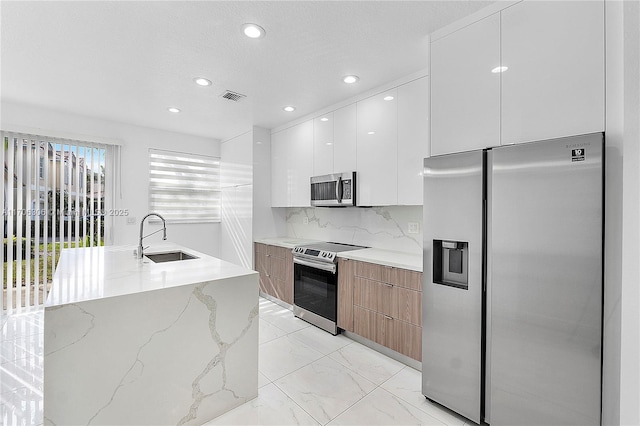 kitchen featuring tasteful backsplash, light stone counters, stainless steel appliances, sink, and white cabinets