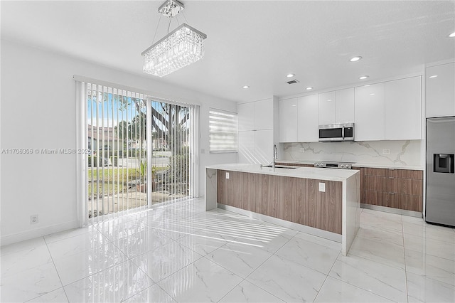 kitchen with white cabinetry, an island with sink, sink, hanging light fixtures, and stainless steel appliances