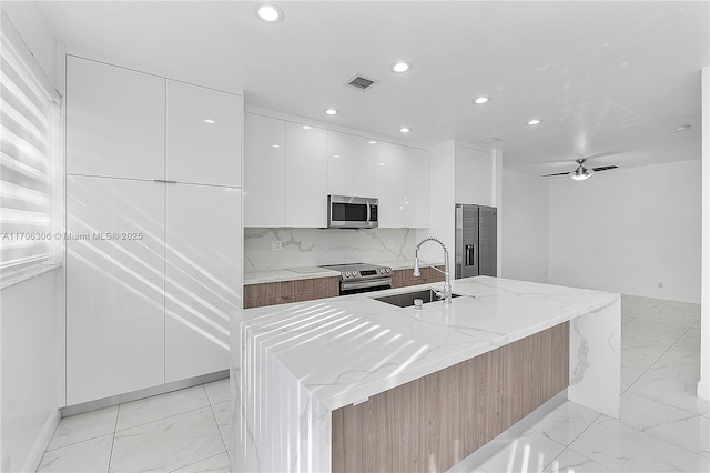 kitchen with appliances with stainless steel finishes, white cabinetry, sink, and a large island with sink