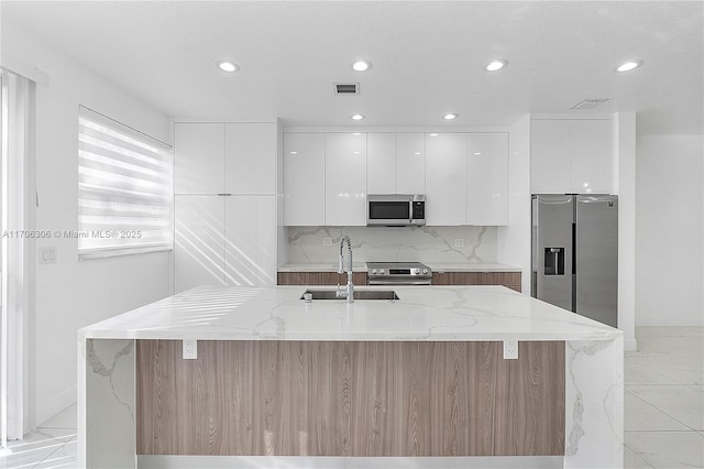 kitchen with stainless steel appliances, light stone countertops, a kitchen island with sink, and white cabinets