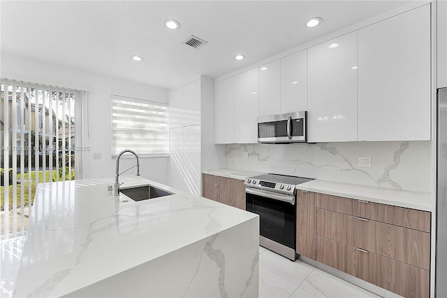 kitchen featuring light stone countertops, appliances with stainless steel finishes, tasteful backsplash, sink, and white cabinets