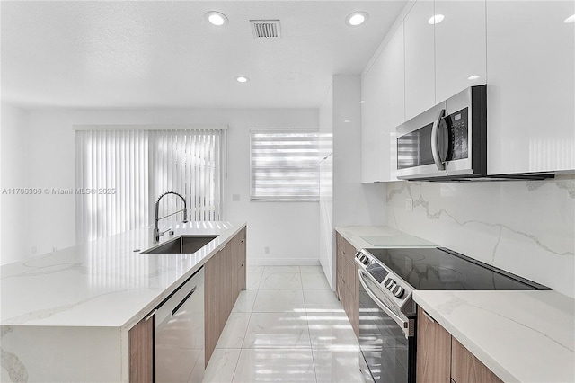 kitchen with light stone countertops, appliances with stainless steel finishes, tasteful backsplash, sink, and white cabinetry