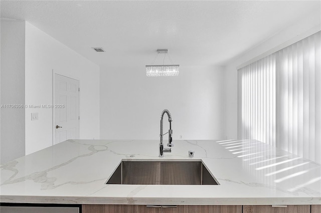 kitchen with a chandelier, pendant lighting, light stone counters, and sink