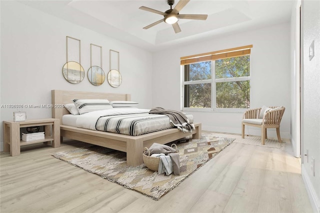 bedroom featuring a tray ceiling, ceiling fan, and light hardwood / wood-style flooring