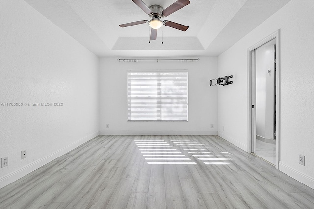 empty room with ceiling fan, light hardwood / wood-style flooring, and a tray ceiling