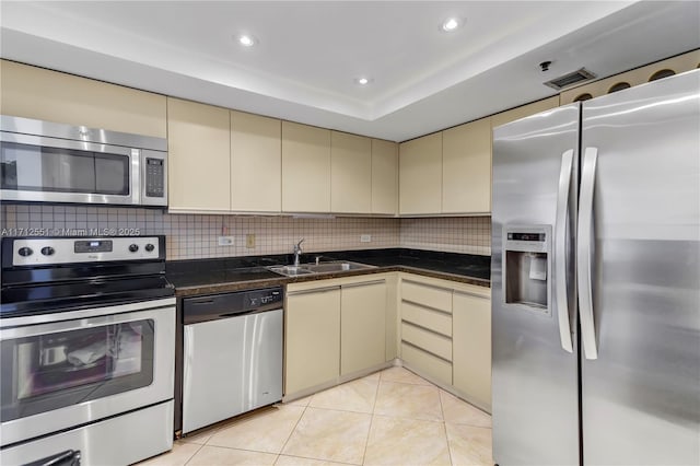 kitchen with light tile patterned flooring, tasteful backsplash, sink, stainless steel appliances, and cream cabinetry