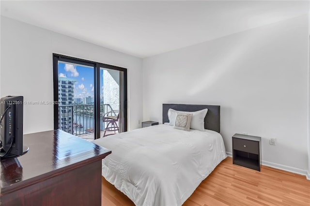 bedroom with access to outside, a city view, baseboards, and wood finished floors