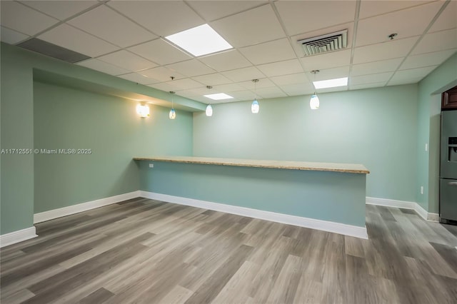 basement featuring stainless steel fridge with ice dispenser, wood-type flooring, and a paneled ceiling