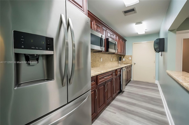 kitchen with sink, appliances with stainless steel finishes, tasteful backsplash, light stone counters, and light wood-type flooring