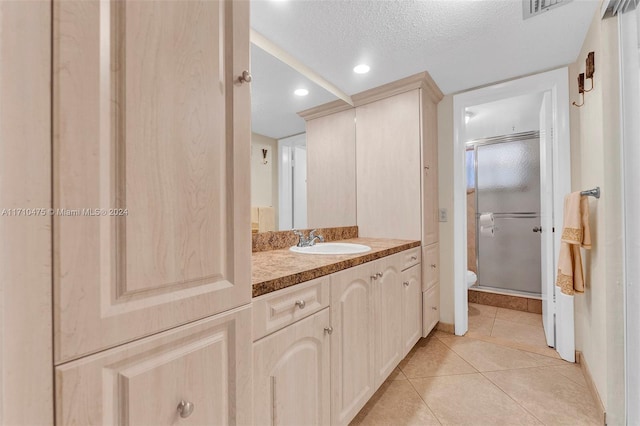 bathroom with vanity, a textured ceiling, a shower with door, tile patterned flooring, and toilet