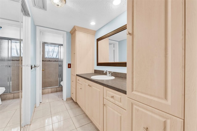 bathroom featuring tile patterned floors, a textured ceiling, toilet, a shower with door, and vanity