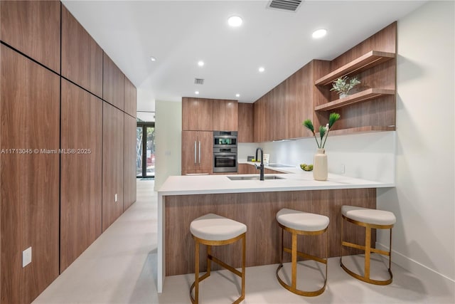 kitchen featuring sink, kitchen peninsula, a kitchen breakfast bar, and double oven