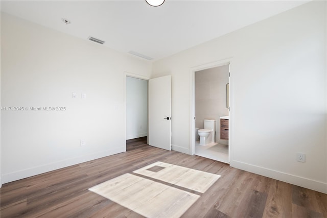 unfurnished bedroom featuring hardwood / wood-style floors and ensuite bath