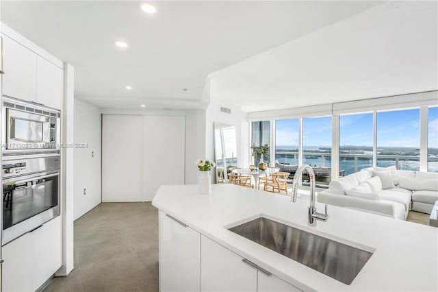 kitchen with sink, stainless steel appliances, white cabinetry, and a water view