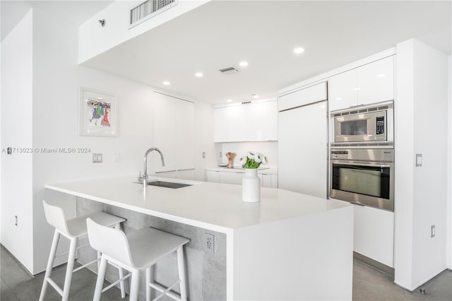 kitchen with built in appliances, white cabinetry, sink, and a breakfast bar