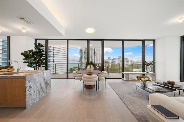 dining space featuring light wood finished floors, a view of city, visible vents, and a wall of windows