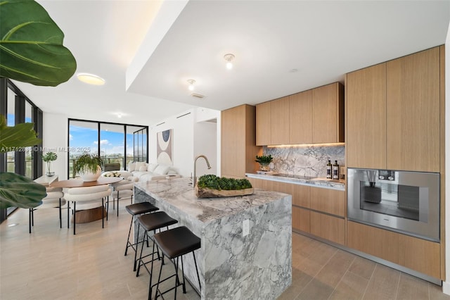 kitchen with stainless steel oven, open floor plan, decorative backsplash, a wall of windows, and modern cabinets