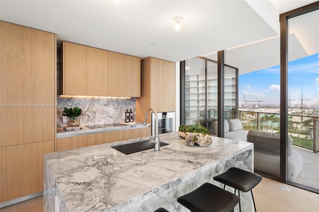 kitchen with light brown cabinets, modern cabinets, a sink, and light stone countertops