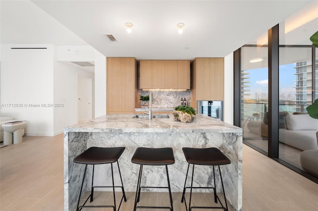 kitchen with visible vents, a breakfast bar, a sink, light stone countertops, and backsplash