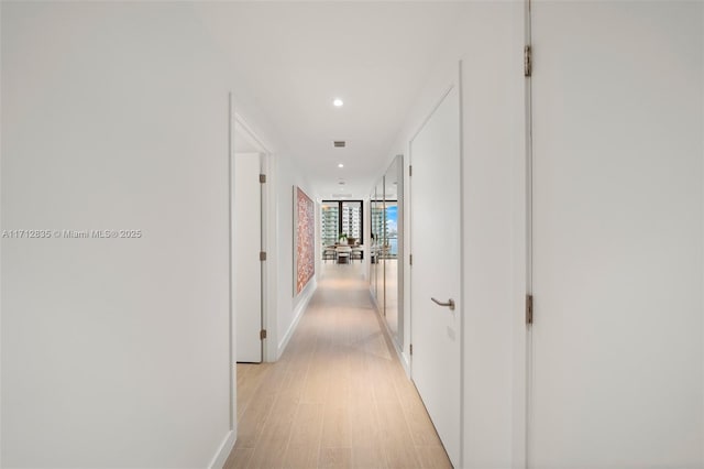 corridor with light wood-style floors, expansive windows, baseboards, and recessed lighting